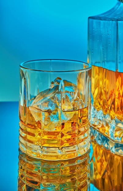 Een glazen en vierkante kristallen karaf met scotch whisky of cognac op de achtergrond op een blauwe achtergrond met kleurovergang met reflectie