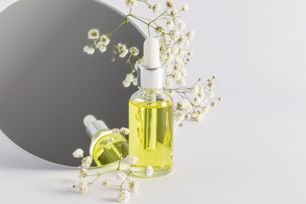 Een glazen fles met een pipet wordt weerspiegeld in een ronde spiegel met een gypsophila vooraanzicht pastel achtergrond presentatie van een cosmetisch product