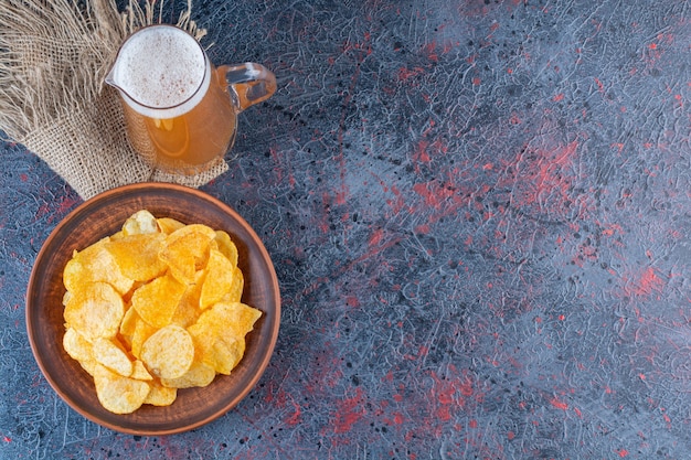 Een glazen pot koud gouden bier met chips op een donkere achtergrond.