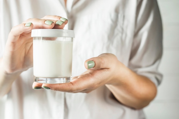 Een glazen pot met een witte deksel met zelfgemaakte yoghurt in de handen van een vrouw