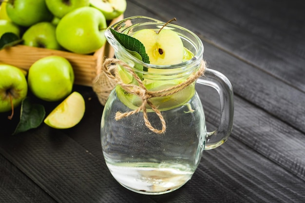 Een glazen pot vers water met appels op de zwarte houten achtergrond. Ruimte kopiëren. Gezond eten, ontgiften