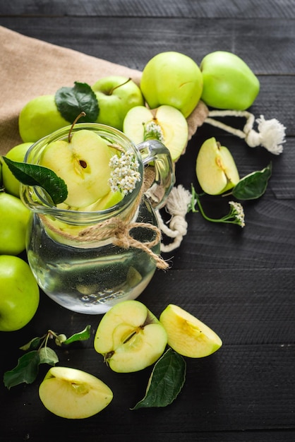 Een glazen pot vers water met appels op de zwarte houten achtergrond. Ruimte kopiëren. Gezond eten, ontgiften