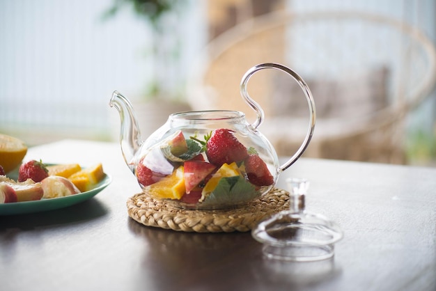 Een glazen theepot met fruit en bessen muntblaadjes op tafel buiten Zomerfruitthee