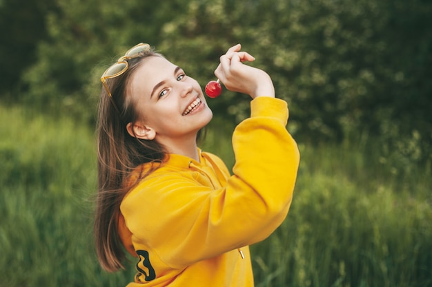 Een glimlachend meisje in een felgele trui heeft een felrode lolly