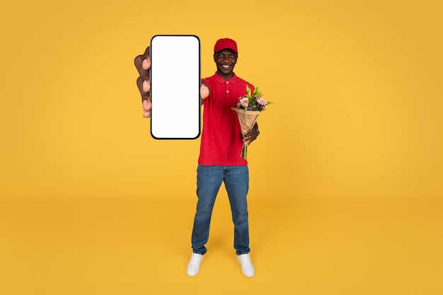 Een glimlachende duizendjarige afro-amerikaanse koerier in uniform houdt een boeket bloemen vast met een lege telefoon