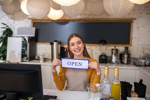 Foto een glimlachende jonge barista die het open teken houdt