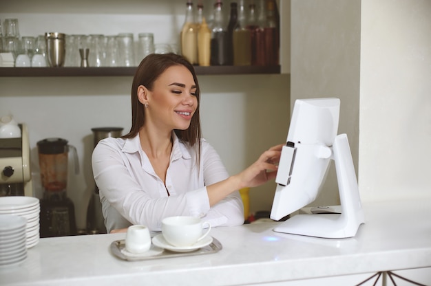 Een glimlachende jonge baristavrouw drukt de bestelling af op de monitor