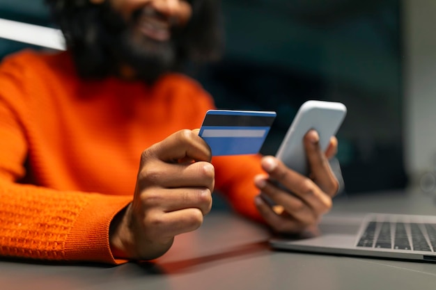 Een glimlachende man met een creditcard en een telefoon.