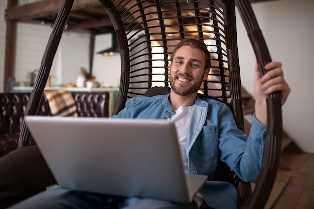 Een glimlachende man werkt op afstand in een comfortabele fauteuil