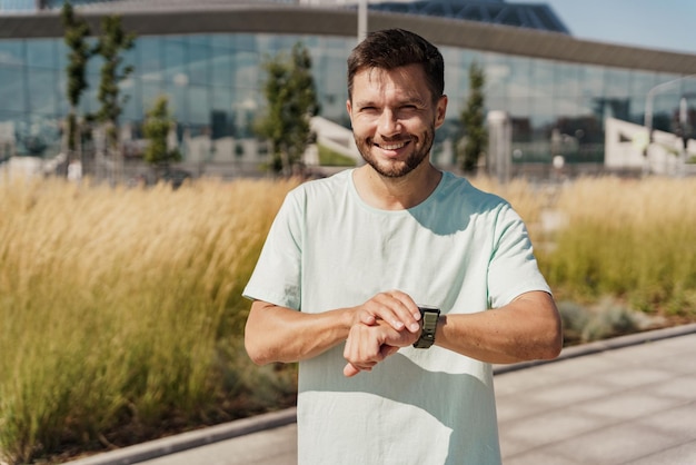 Een glimlachende mannelijke atleet gebruikt een fitness horloge buiten trainen in sportkleding gezonde levensstijl mentale