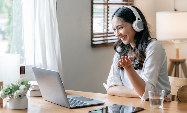 Een glimlachende onderneemster die met hoofdtelefoon naar laptop webcam kijkt, maakt thuis een zakelijk conferentiegesprek