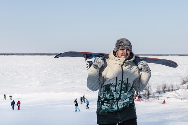 Een glimlachende snowboarder beklimt een besneeuwde helling met een snowboard op zijn schouder Een gelukkige man op vakantie in een skigebied Extreme sportrecreatie