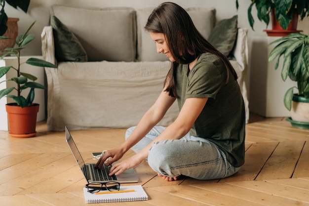 Een glimlachende student die op de vloer zit en een laptop gebruikt voor online leren