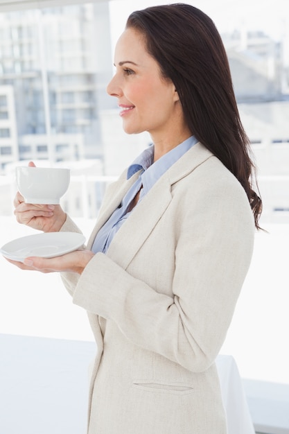 Een glimlachende vrouw die een kop in een bureau houdt