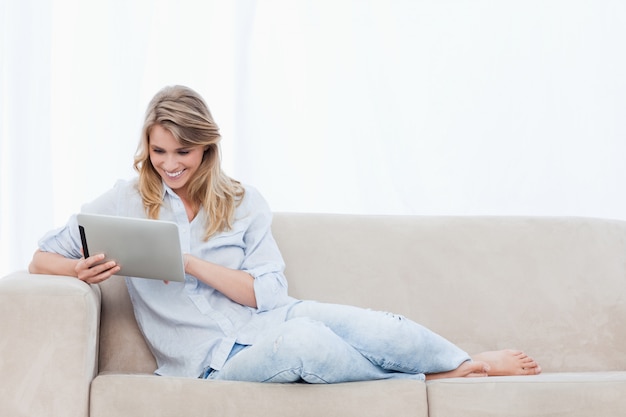 Een glimlachende vrouw die een tablet houdt zit op een laag