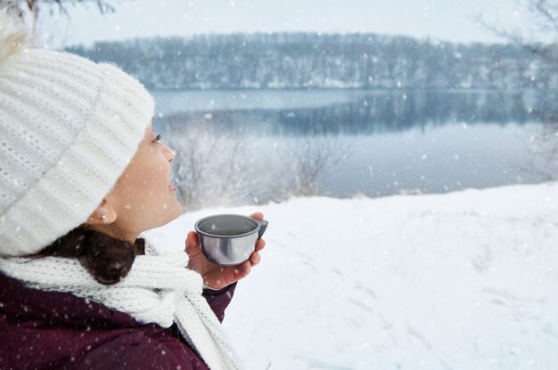 Foto een glimlachende vrouw in witte gebreide muts en sjaal wegkijken en genieten van mooie besneeuwde dag