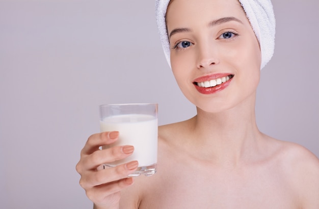 Een glimlachende vrouw met een handdoek op haar hoofd houdt een glas melk.