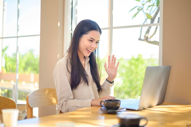 Een glimlachende zakenvrouw in oortelefoons die webinar op laptop bekijkt en een videogesprek voert op de werkplek