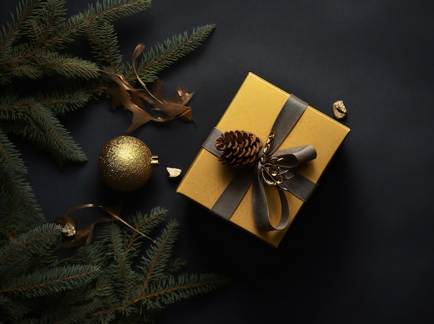 Een gouden kerstcadeau met een gouden strik zit op een donkere achtergrond met dennennaalden.