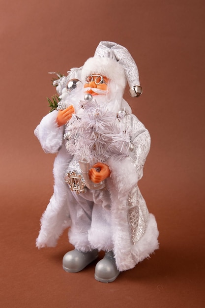 Foto een grappig kerstmanspeelgoed met een zak met cadeautjes op zijn rug en een kerstboom in zijn hand en een witte broek