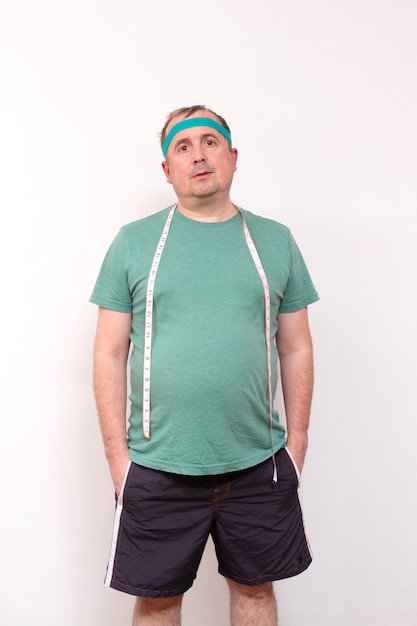 Een grappige dikke man in een groene bandana en een shirt met een meetlint om zijn nek thuis fitness training onafhankelijke training