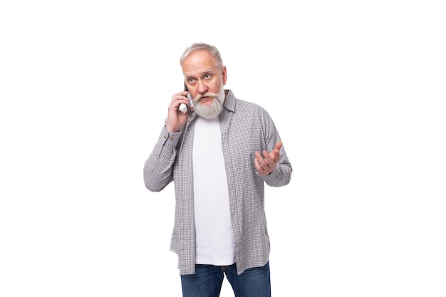 Een grijsharige oudere man in een shirt die op een mobiele telefoon chat op een witte achtergrond met kopieerruimte