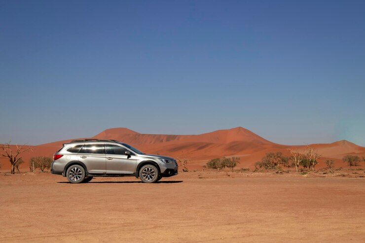 Een grijze Subaru Outback bij een rode zandduin op een hete zonnige dag