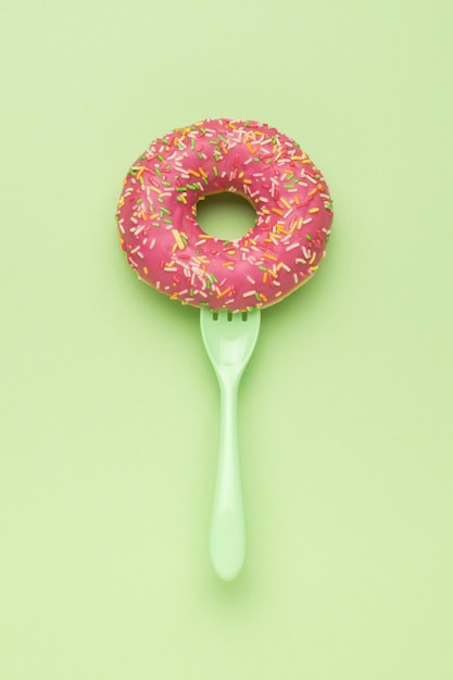 Een groene vork in een rode donut op een groene achtergrond Het minimale concept van populair bakken