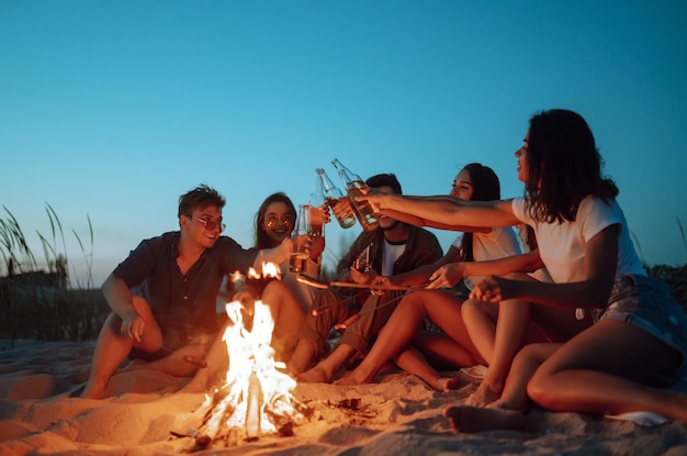 Een groep gelukkige vrienden proost en drinkt bier op het strand, genietend van vakantie Vakantietijd lachen