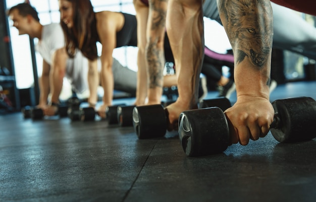 Een groep gespierde atleten die trainen in de sportschool. Gymnastiek, training, flexibiliteit voor fitnesstraining. Actieve en gezonde levensstijl, jeugd, bodybuilding. Close up van handen met gewichten opleiding.