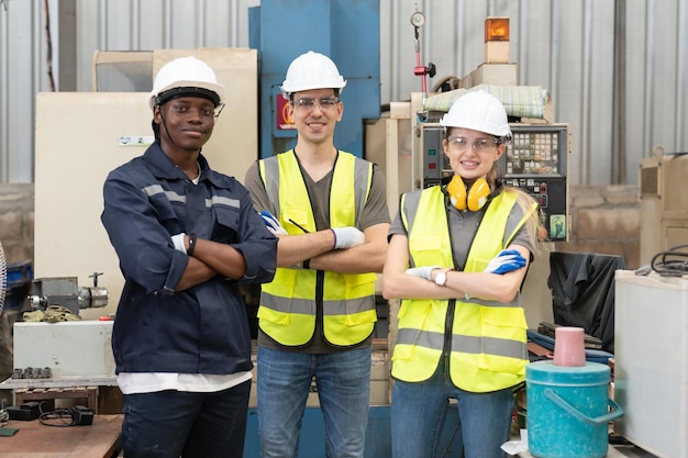 Een groep ingenieurs draagt helmen, veiligheidsarmen gekruist in de werkplaats van de fabriek