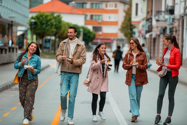 Een groep jonge mensen gekleed in moderne kleding praat terwijl ze door de stad lopen en snoep eten Selectieve focus Foto van hoge kwaliteit