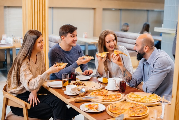 Een groep jonge vrolijke vrienden zit in een café te praten en pizza te eten