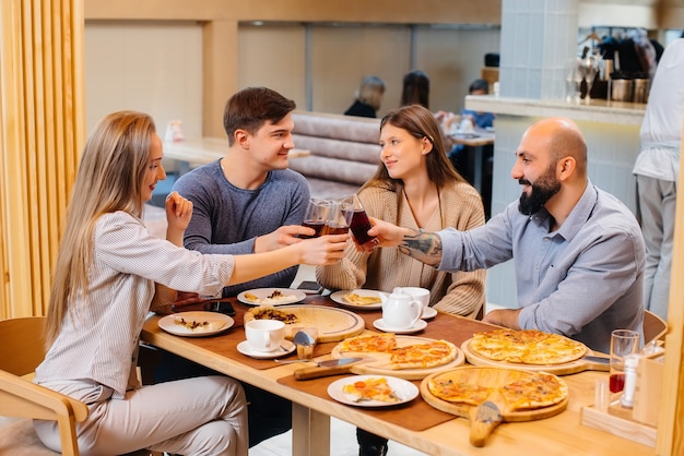 Een groep jonge vrolijke vrienden zit in een café te praten en pizza te eten