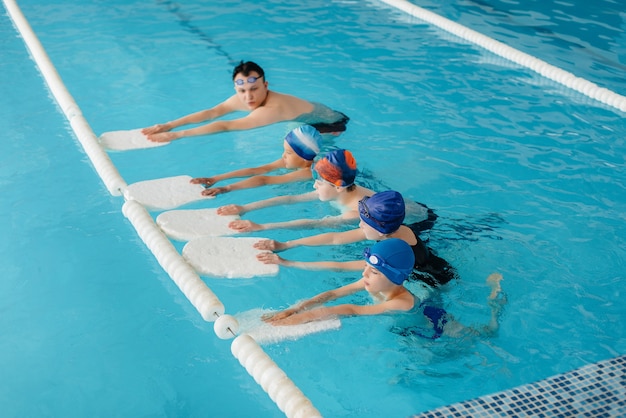 Een groep jongens en meisjes trainen en leren zwemmen in het zwembad met een instructeur. Ontwikkeling van kindersporten.
