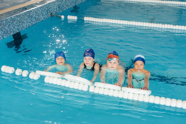 Een groep jongens en meisjes trainen en leren zwemmen in het zwembad met een instructeur. Ontwikkeling van kindersporten.