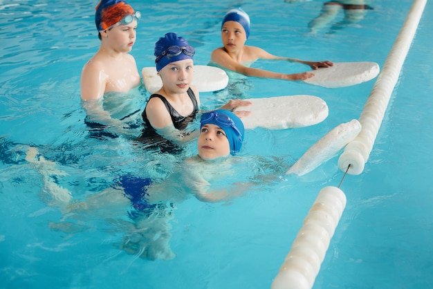 Een groep jongens en meisjes trainen en leren zwemmen in het zwembad met een instructeur. ontwikkeling van kindersporten.