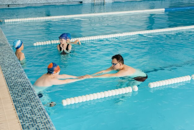 Een groep jongens en meisjes trainen en leren zwemmen in het zwembad met een instructeur. Ontwikkeling van kindersporten.