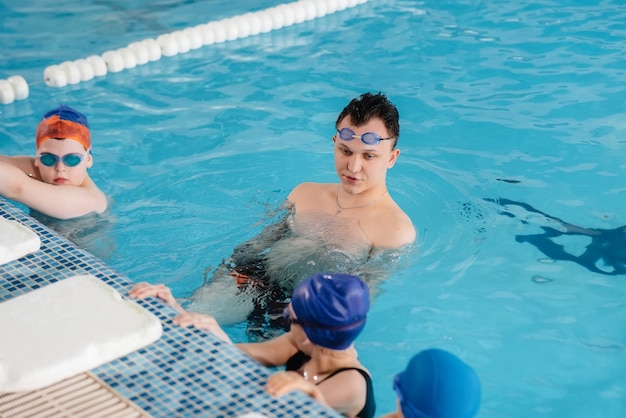 Een groep jongens en meisjes trainen en leren zwemmen in het zwembad met een instructeur. Ontwikkeling van kindersporten.