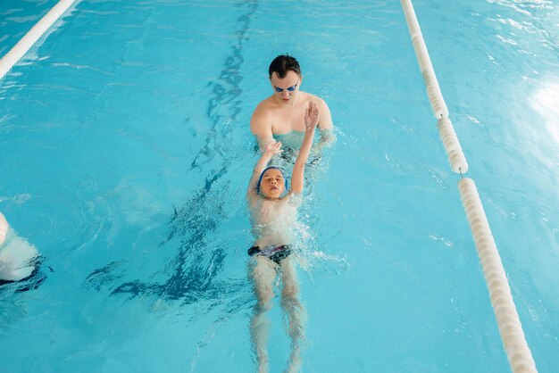 Een groep jongens en meisjes trainen en leren zwemmen in het zwembad met een instructeur. Ontwikkeling van kindersporten.