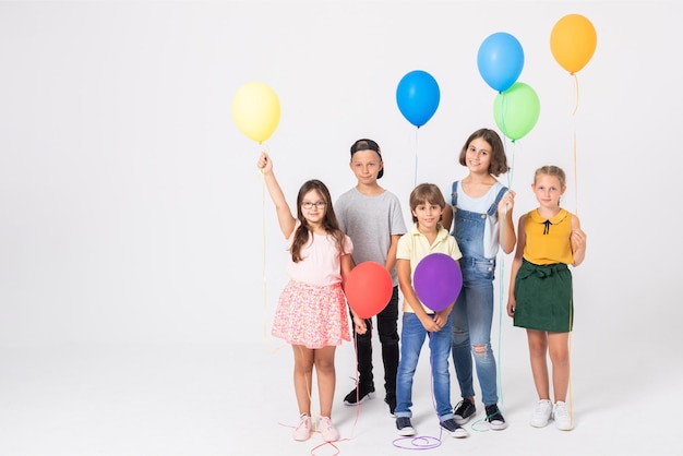 Een groep kinderen met ballonnen voor een witte achtergrond.