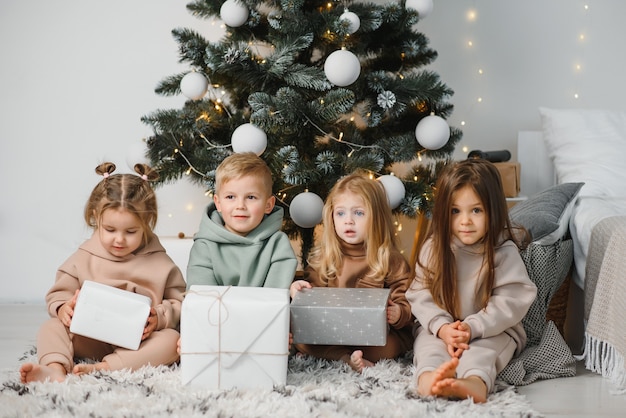 Een groep kinderen onder een kerstboom thuis. Jongens en meisjes in fancy kostuums vieren wintervakanties. Kinderen openen cadeautjes bij de open haard.