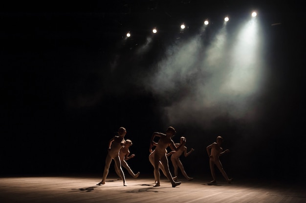 Een groep kleine balletdansers repeteert op het podium met licht en rook