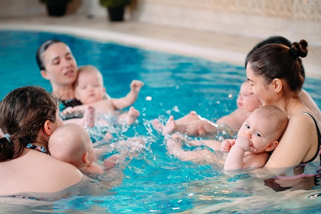 Een groep moeders met hun jonge kinderen in een kinderzwemles met een coach.