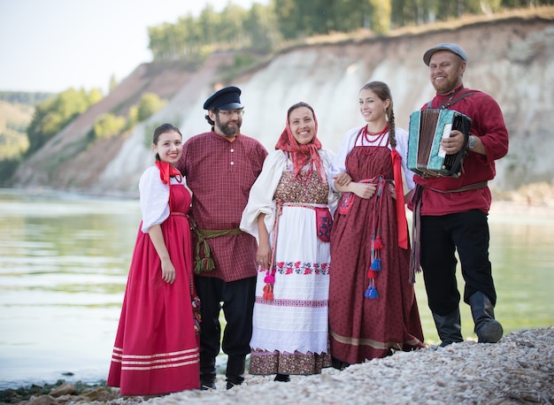 Een groep mooie mensen in het Russische nationale kostuum die op de achtergrond van water staat, glimlachend