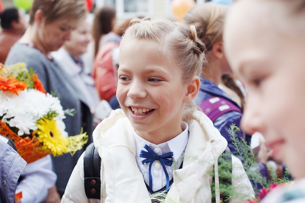 Een groep schoolmeisjes met strikken, met bloemen gaat op vakantie voor onderwijs, glimlach en verheugt zich.