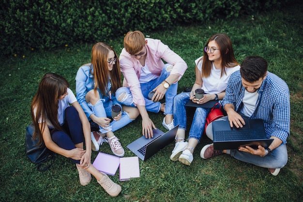 Foto een groep studenten zit op een campus. cursuswerk herhalen op een laptop. zittend op het gras.