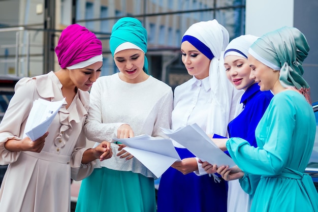 Een groep van vijf jonge en aantrekkelijke zakenvrouwen in moslimkleding veelkleurige hijab en een tulband die de werkende laptop bedekt en communiceert en funteam werk en succesconcept heeft