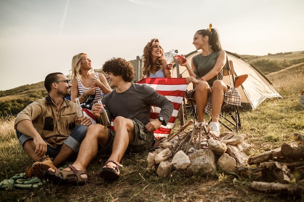 Een groep vrolijke vrienden die op een festival buiten hun tent zitten en genieten van een drankje.