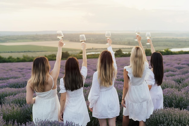 Een groep vrouwen in witte jurken houdt wijnglazen omhoog voor een lavendelveld.